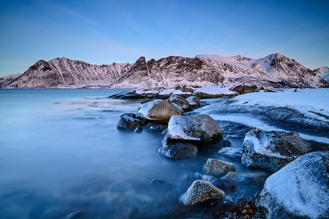 Vereiste Felsen in Meeresbucht mit verschneiten Bergen, Lofoten, Nordland, Norwegen