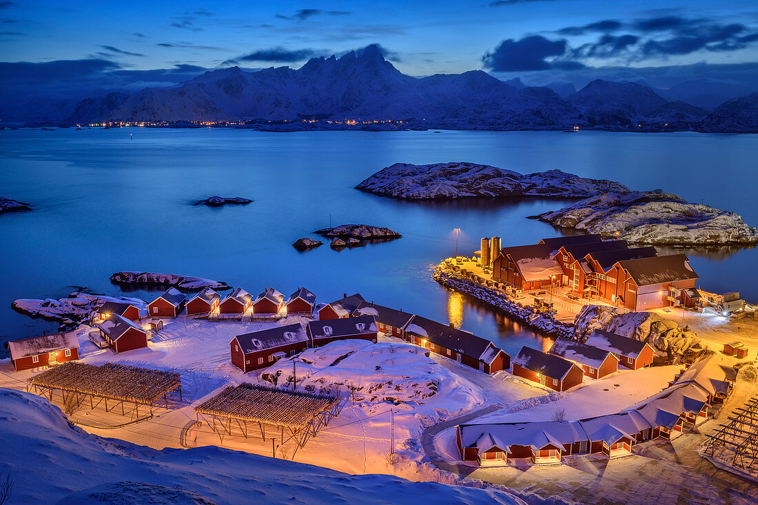 Beleuchteter Hafen von Mortsund mit norwegischen roten Fischerhäusern, Mortsund, Lofoten, Nordland, Norwegen