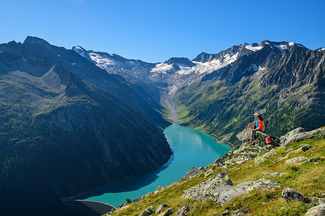 Man and woman sit on rocks and look at Schlegeisspeicher and Großer Möseler, Peter-Habeler-Runde, Zillertal Alps, Tyrol, Austria