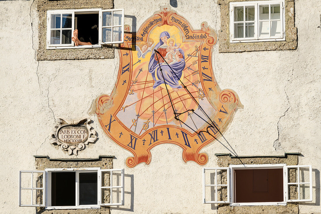 Sundial on house wall and feet of a person sunbathing, Salzburg, Austria