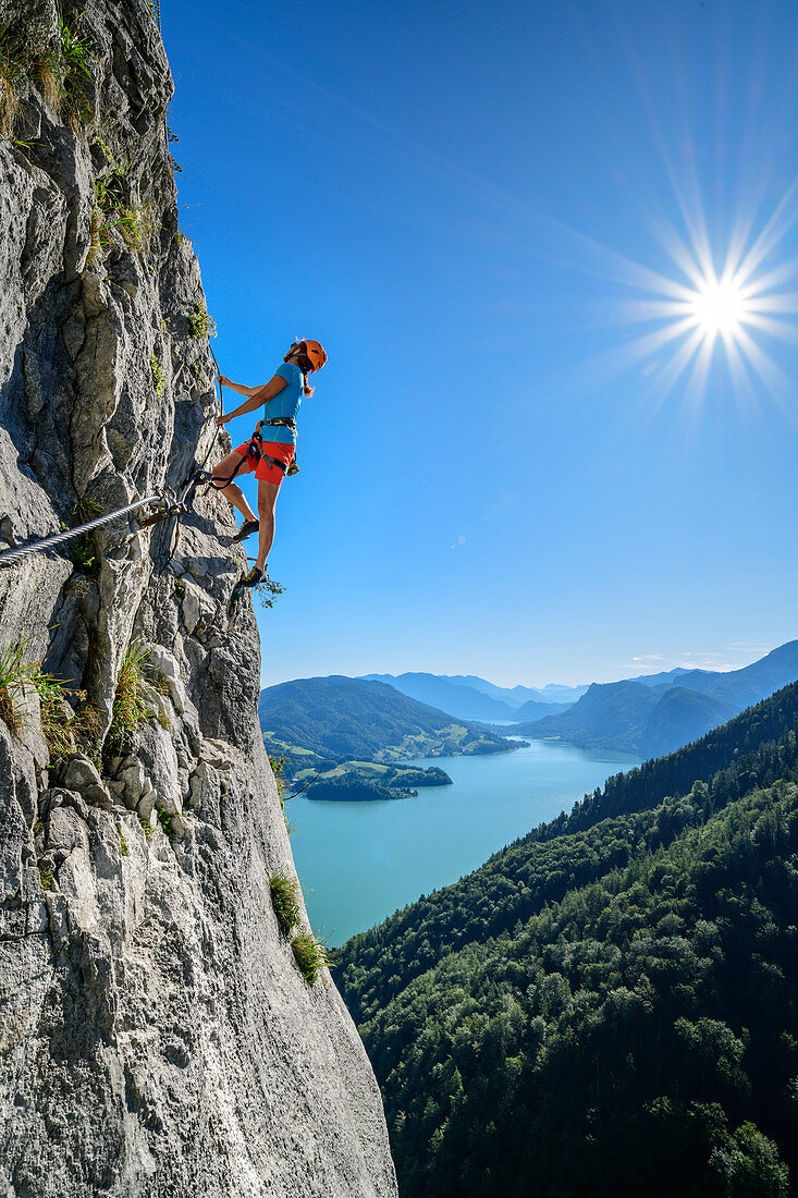 Woman climbs via ferrata on Drachenwand, Mondsee in the background, Drachenwand, Mondsee, Salzkammergut, Salzburg, Austria
