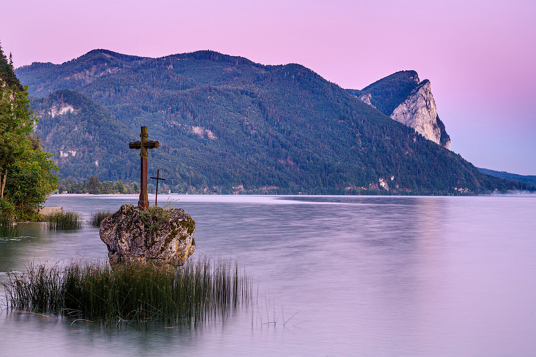 Fels mit Kreuz im Mondsee bei Morgendämmerung, Drachenwand im Hintergrund, Mondsee, Salzkammergut, Salzburg, Österreich