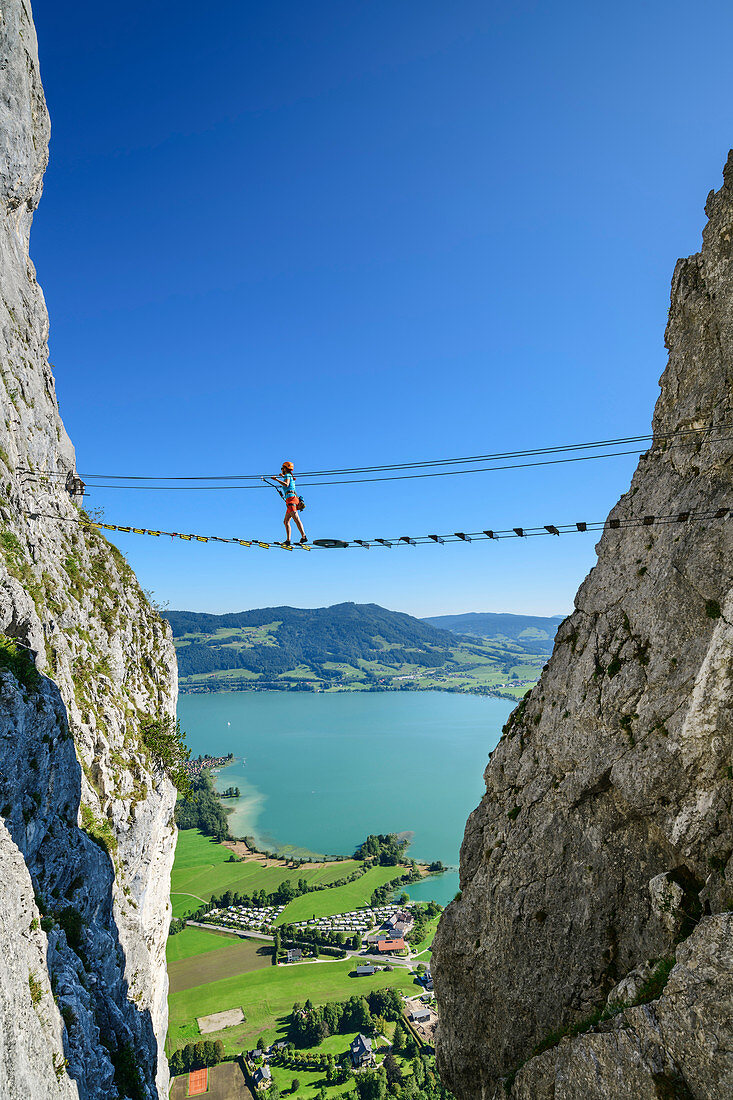 Frau geht auf Klettersteig über Hängebrücke, Klettersteig Drachenwand, Mondsee im Hintergrund, Drachenwand, Mondsee, Salzkammergut, Salzburg, Österreich