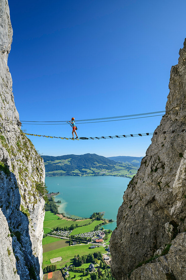 Woman walks on via ferrata over suspension bridge, via ferrata Drachenwand, Mondsee in the background, Drachenwand, Mondsee, Salzkammergut, Salzburg, Austria
