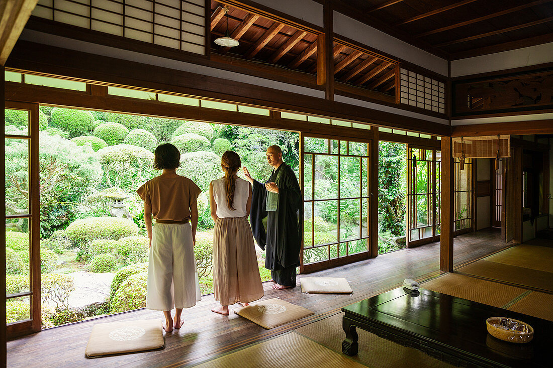 Buddhistischer Priester und zwei japanische Frauen stehen im einem buddhistischen Tempel