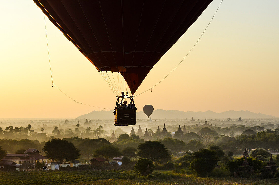 Hot air balloon over landscape with temples at sunset, Bagan, Myanmar.