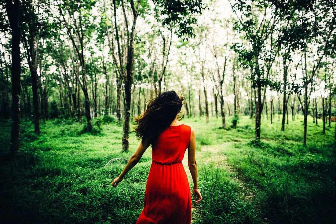 Rear view of young woman wearing red dress running in a forest.