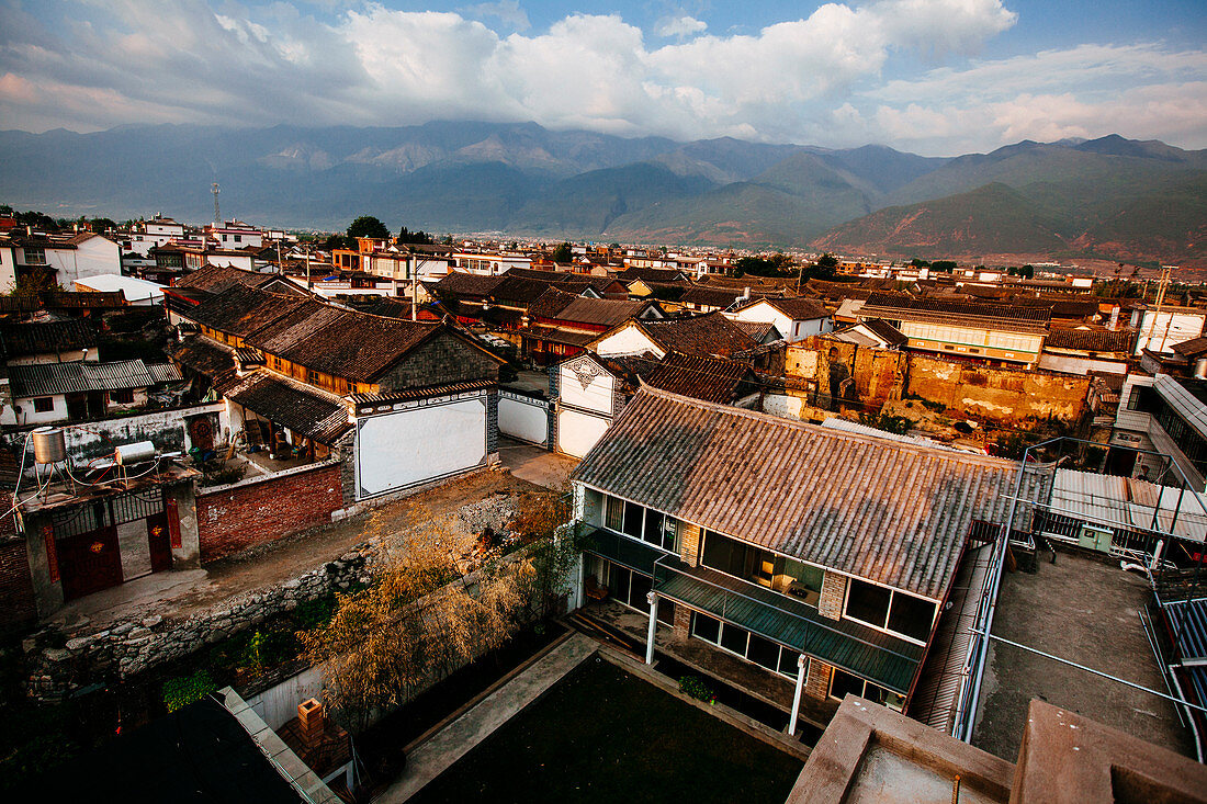High angle view across rooftops of traditional Asian houses, mountains in the distance.