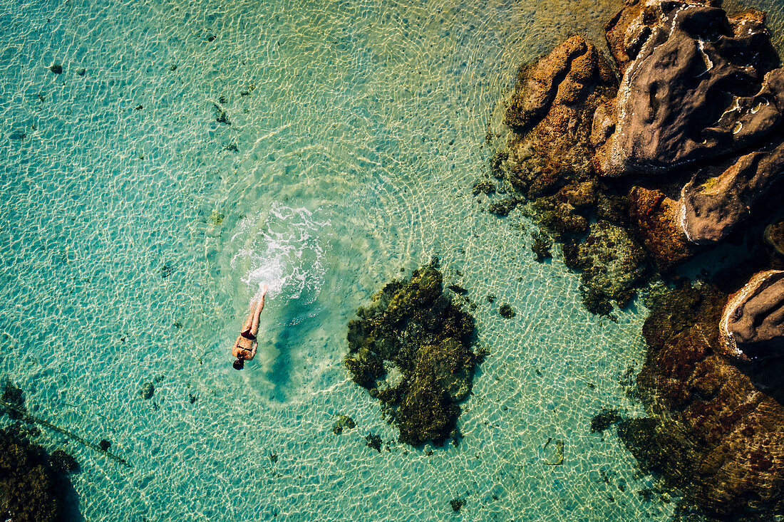 High angle view of woman swimming in the ocean in between rocks.