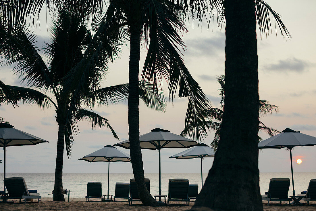 Sonnenschirme am Strand in einem Luxusresort auf einer tropischen Insel bei Sonnenuntergang