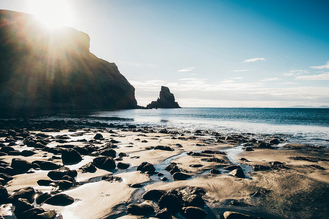 Sandy beach with rocks and cliff, rugged ocean coast.