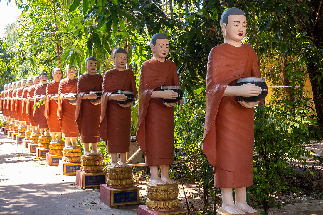 Reihe buddhistischer Mönchsstatuen mit roten Gewändern und Almosenschalen in den Gärten des buddhistischen Tempels in Siem Reap
