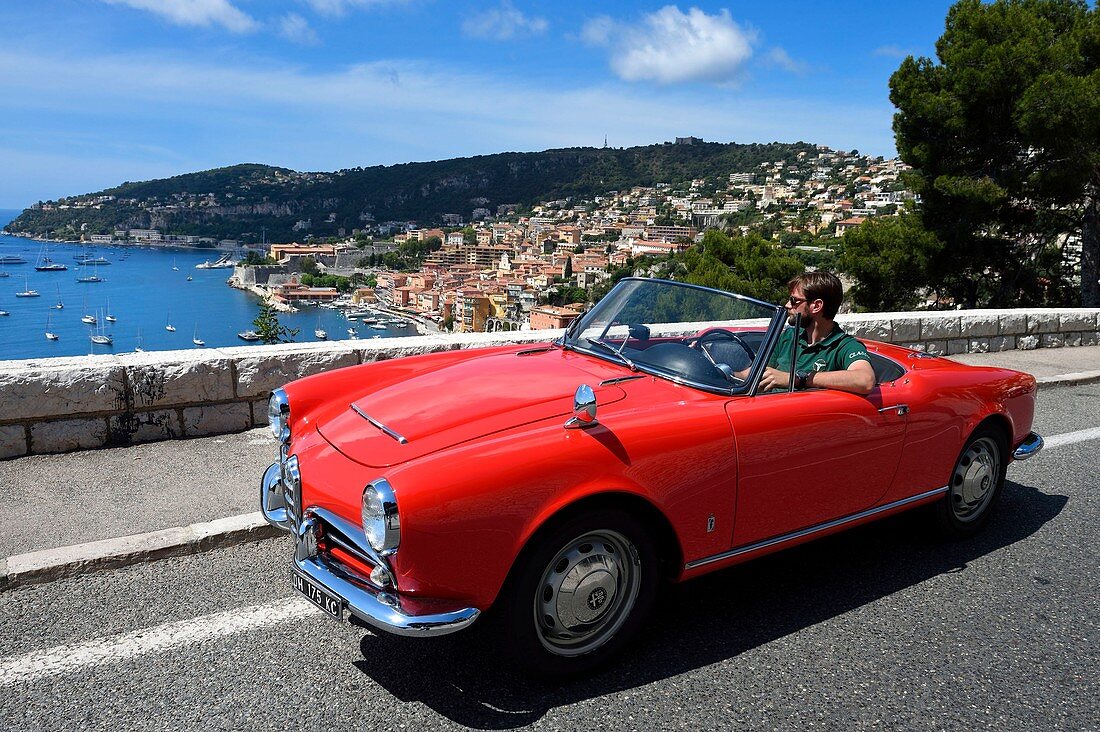 Frankreich, Alpes Maritimes, Villefranche sur Mer, Alfa Romeo Giulietta Cabriolet auf der Straße Basse Corniche mit Blick auf die Stadt, (Obligatorische Erwähnung: Firma 'Rent a Classic Car')