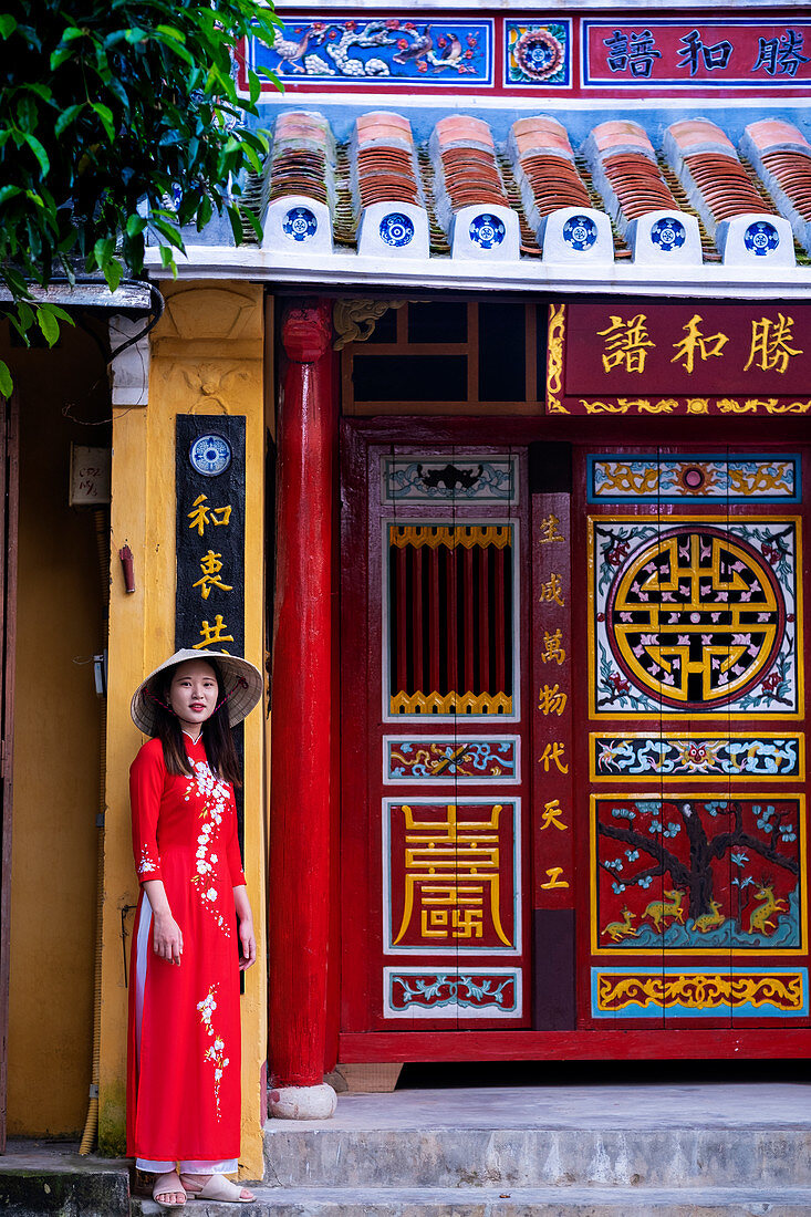 Eine junge Vietnamesin in traditioneller Ao-Dai-Kleidung vor einem Tempel im historischen Stadtzentrum, Hoi An, Vietnam, Indochina, Südostasien, Asien