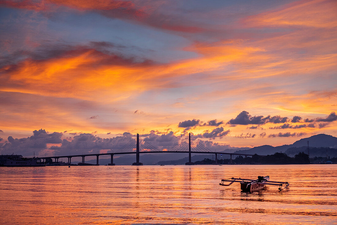 Sunset over the harbour in Ambon city showing the suspension bridge and an outrigger boat, Ambon, Moluccas (Maluku), Indonesia, Southeast Asia, Asia