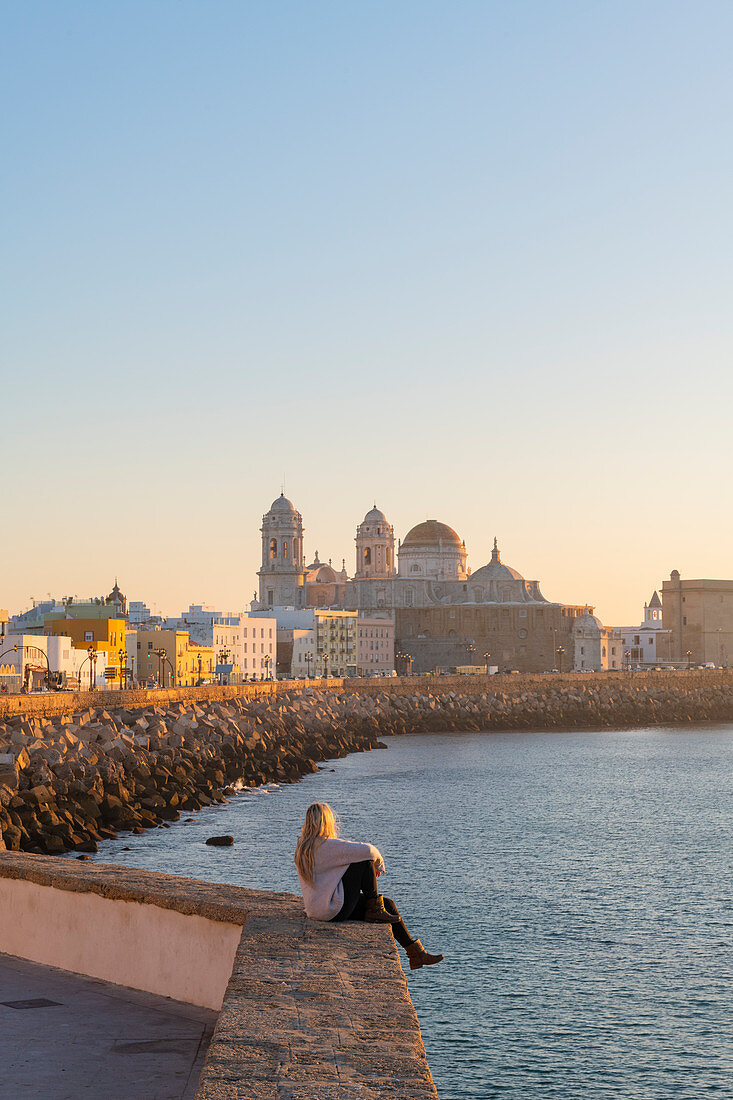 Frau blickt von der Uferpromenade auf die Kathedrale Santa Cruz und den Ozean, Cádiz, Andalusien, Spanien, Europa