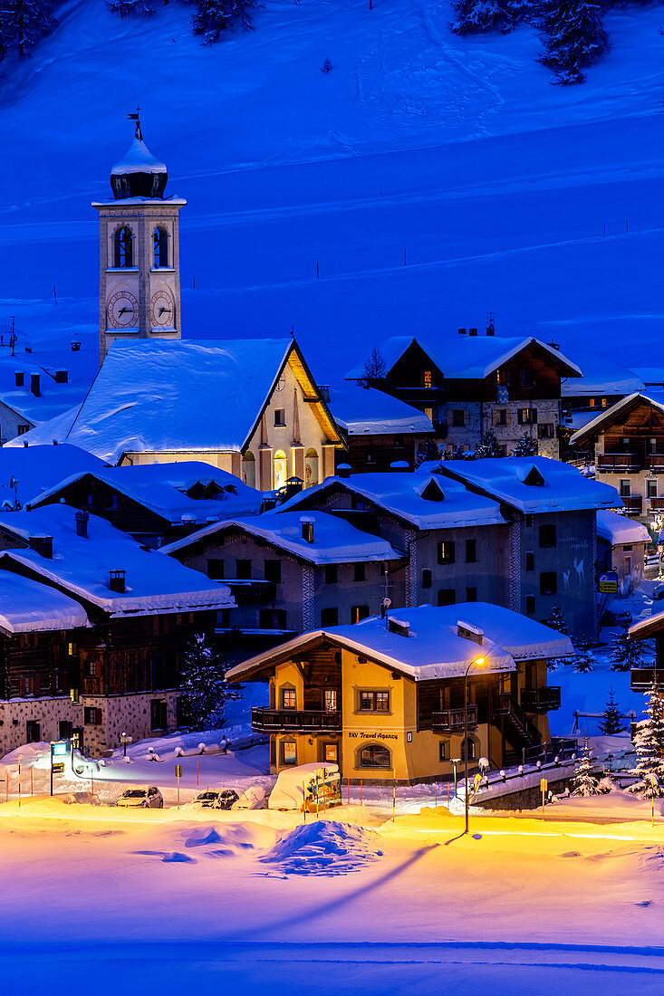 Kirche und Häuser beleuchtet während einer Winterdämmerung, Livigno, Valtellina, Lombardei, Italien, Europa