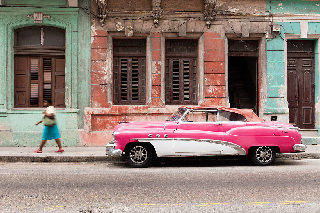 Woman walks past a pink and white vintage car, parked on street in Havana, Cuba, West Indies, Caribbean, Central America
