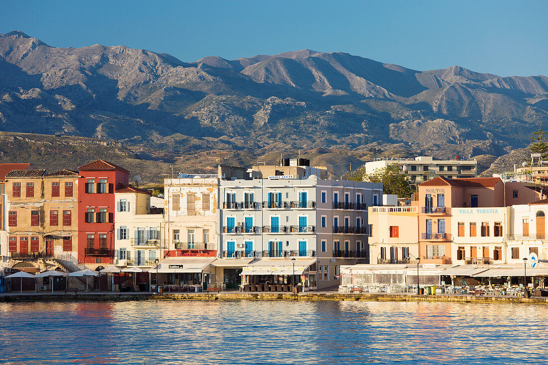 Blick über den venezianischen Hafen zu bunten Gebäuden am Wasser unter dem Lefka Ori, Hania (Chania), Kreta, griechischen Inseln, Griechenland, Europa