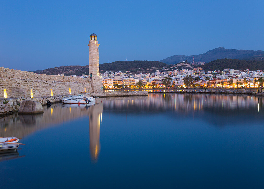 View across the Venetian Harbour at dusk, 16th century lighthouse reflected in water, Rethymno (Rethymnon), Crete, Greek Islands, Greece, Europe