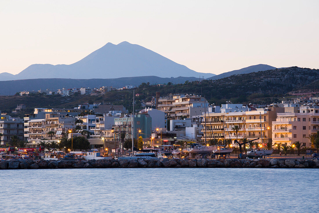 Seafront buildings illuminated at dawn, Mount Psiloritis, aka Mount Ida, in background, Rethymno (Rethymnon), Crete, Greek Islands, Greece, Europe