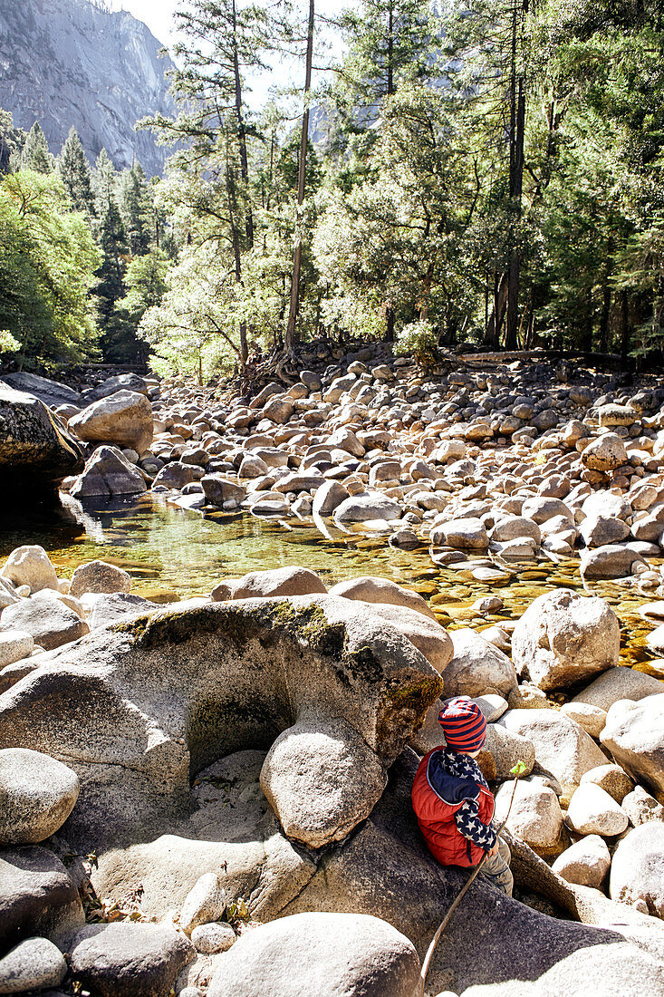 Child plays on the Merced River stones in Yosemite Park. California, United States.