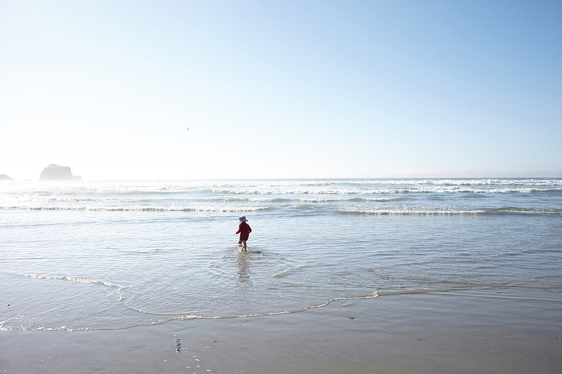 Kind mit Hut läuft ins Wasser am Strand von Big Sur, Kalifornien, USA