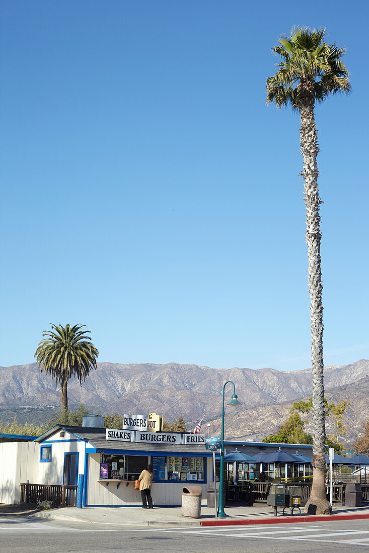 Burgerrestaurant mit Palmen vor Bergen und blauem Himmel, Carpinteria, Kalifornien, USA