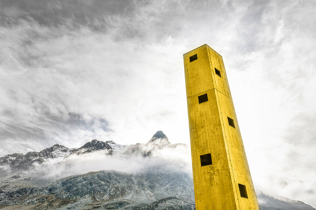 Yellow Origen Tower looms in the sky with mountains in the background. Julier Pass, Graubünden, Switzerland, Europe