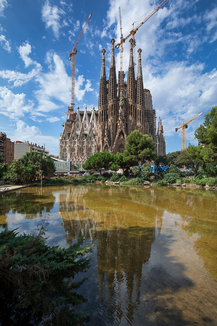 Kathedrale von Gaudi Sagrada Familia von außen mit Spiegelung im Wasser bei Sonne, Barcelona, Spanien\n