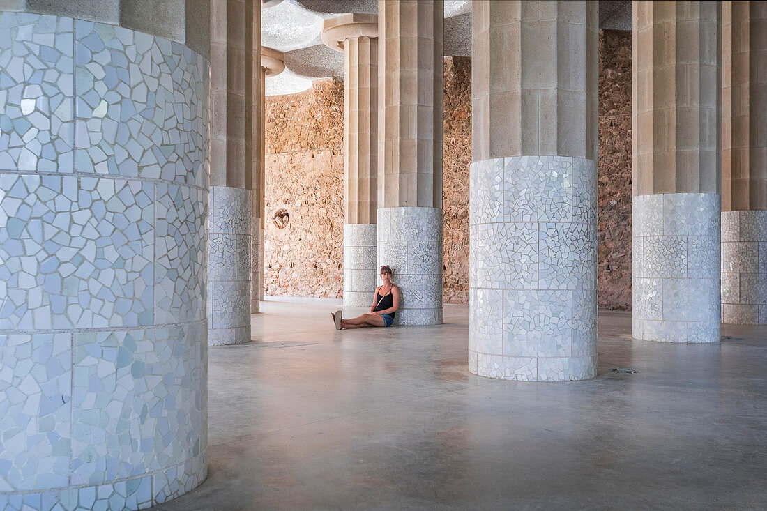 Frau sitzt im Sala Hipostila an Steinsäulen im Park Guell, Barcelona