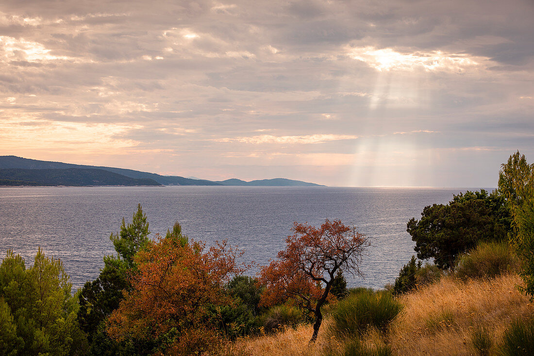 Küste von Brac bei Bol mit Meer und Sonnenstrahlen durch Wolken am Nachmittag, Kroatien\n