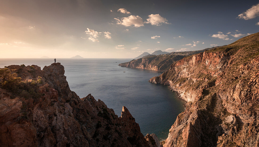 Man on cliff on Lipari rocky coast at sunset, Sicily Italy