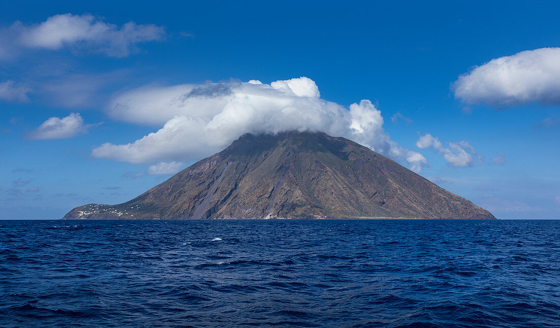Stromboli volcanic island in the sea with clouds at the summit at sun, Sicily Italy