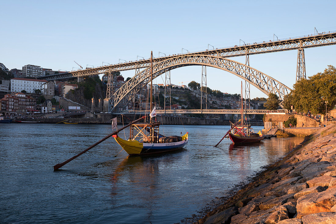 Traditionelle Schiffe auf dem Fluss Douro mit Brücke Ponte Dom Luis I in Porto bei Sonnenuntergang, Portugal\n