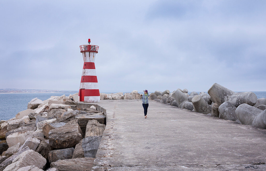 Frau auf Mole und Wellenbrecher am Leuchtturm des Hafens von Peniche, Portugal\n
