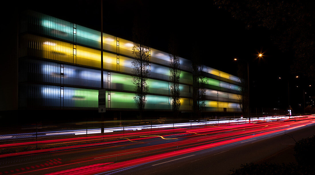 Bunt beleuchtetes Wohnhaus mit Autolichtern bei Nacht, München\n