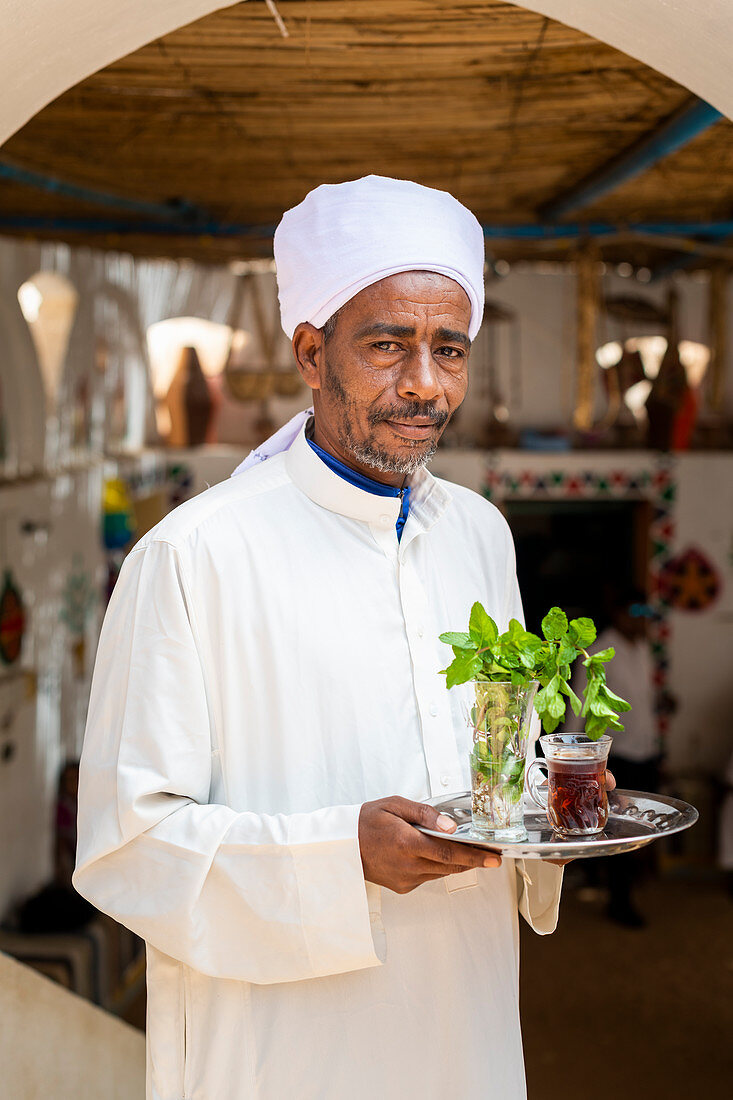 Ein ägyptischer Mann hält ein Tablett mit einem Glas Minztee und einigen frischen Minzblättern, Assuan, Ägypten, Nordafrika, Afrika