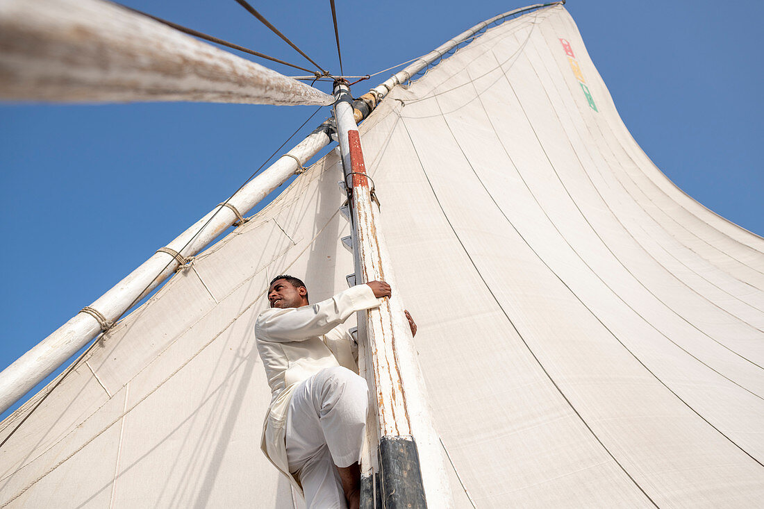 Ein Ägypter klettert auf den Mast eines traditionellen Felucca-Segelboots mit Holzmasten und Baumwollsegeln auf dem Nil, Assuan, Ägypten, Nordafrika, Afrika