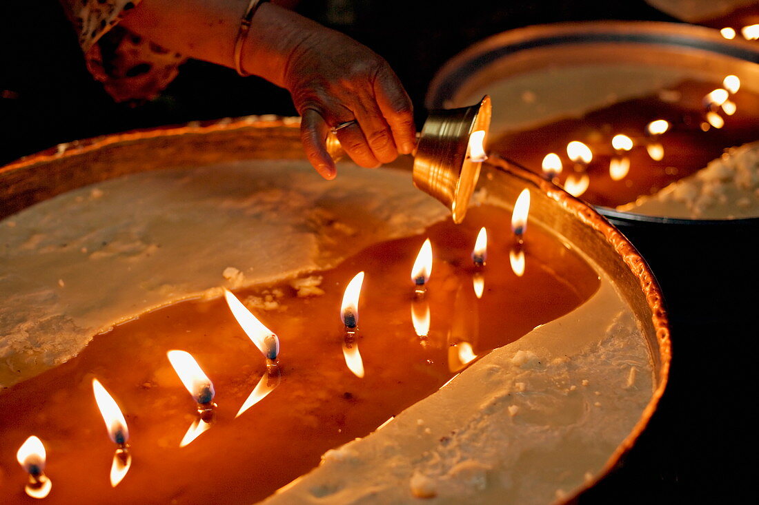 Pilgrims pour melting butter from their lamps into the yak butter lamps in the monastery, topping them up continually, Lhasa, Tibet, China, Asia