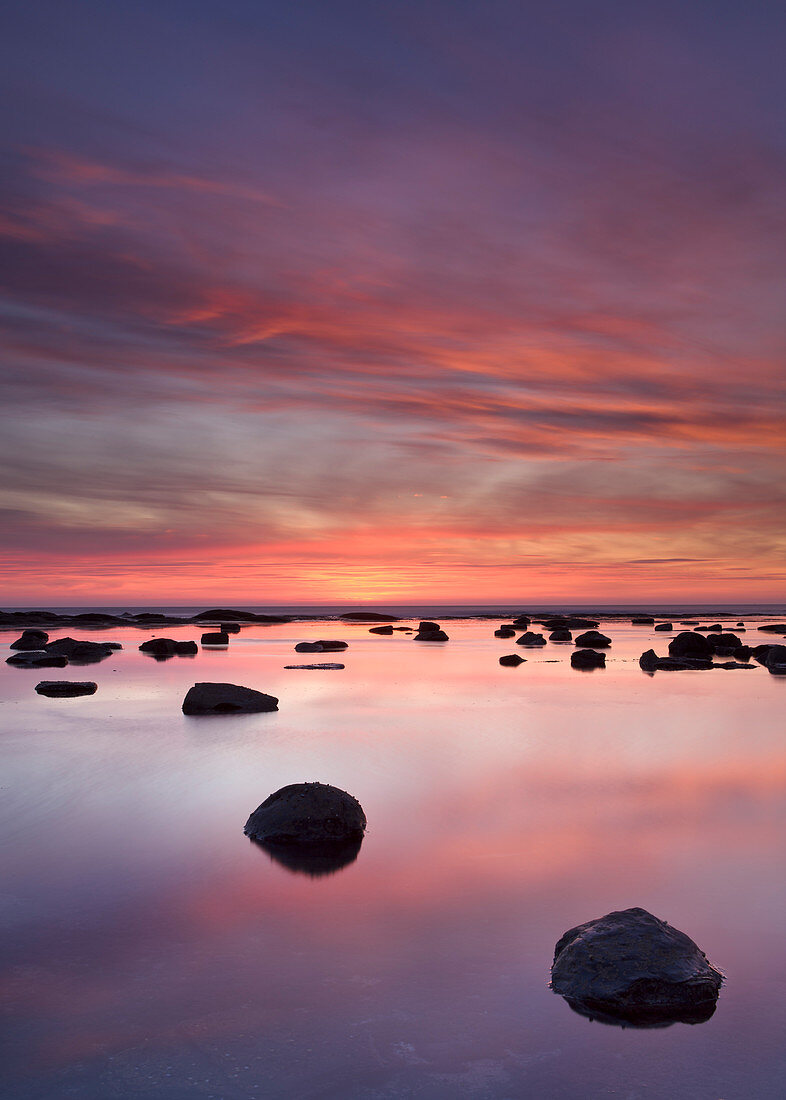 Felsbrocken und Reflexionen im Meer bei Sonnenaufgang, Saltwick Bay, Yorkshire, England, Vereinigtes Königreich, Europa