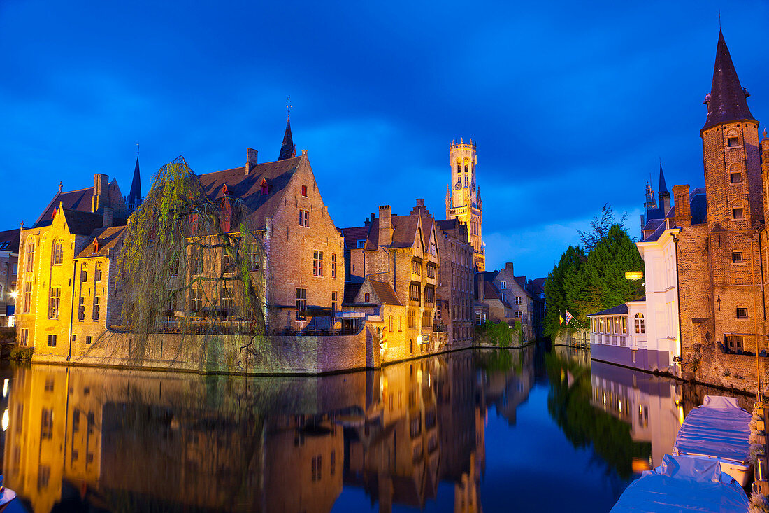 Der Glockenturm und die nachts beleuchteten Gebäude entlang eines Kanals im historischen Zentrum von Brügge, UNESCO-Weltkulturerbe, Belgien, Europa