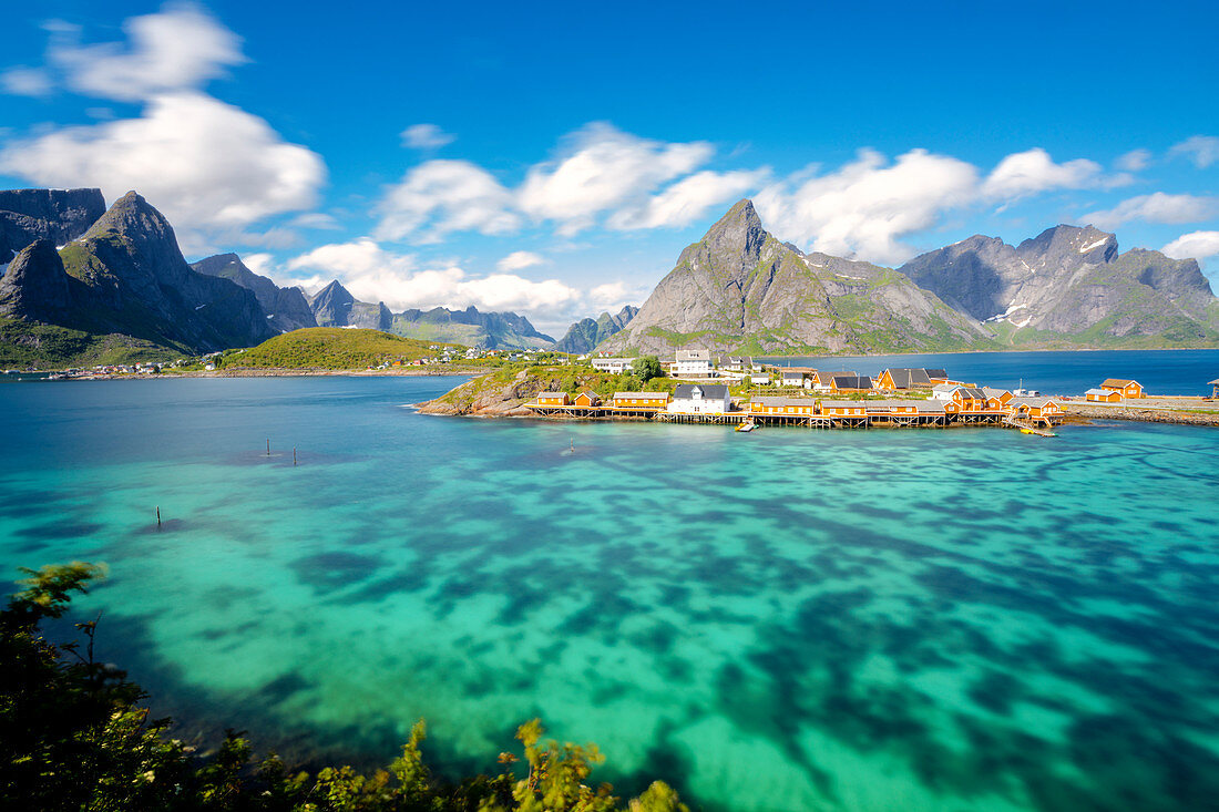 Das türkisfarbene Meer um das typische Fischerdorf, umgeben von felsigen Gipfeln, Sakrisoy, Reine, Moskenesoya, Lofoten, Norwegen, Skandinavien, Europa