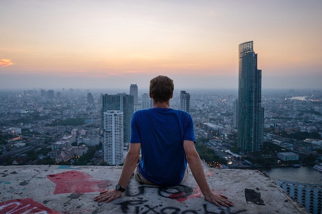 A single man watching sun set over city skyline at dusk, Bangkok, Thailand, Southeast Asia, Asia
