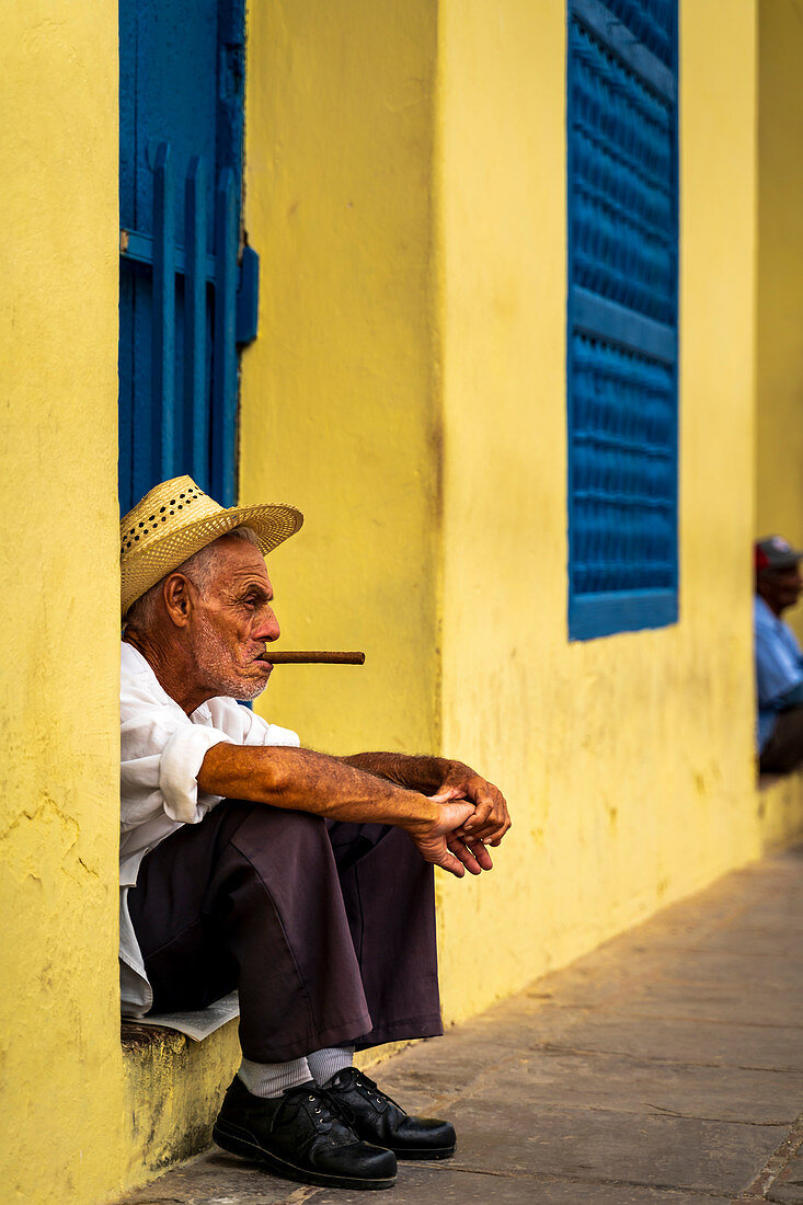 An elderly Cuban sitting on a doorstep, smoking a cigar, Trinidad, Sancti Spiritus Province, Cuba, West Indies, Caribbean, Central America