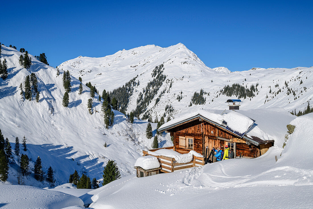 Man and woman on ski tour take a break at alpine pasture, Regenfeldjoch, Kitzbüheler Alpen, Tyrol, Austria