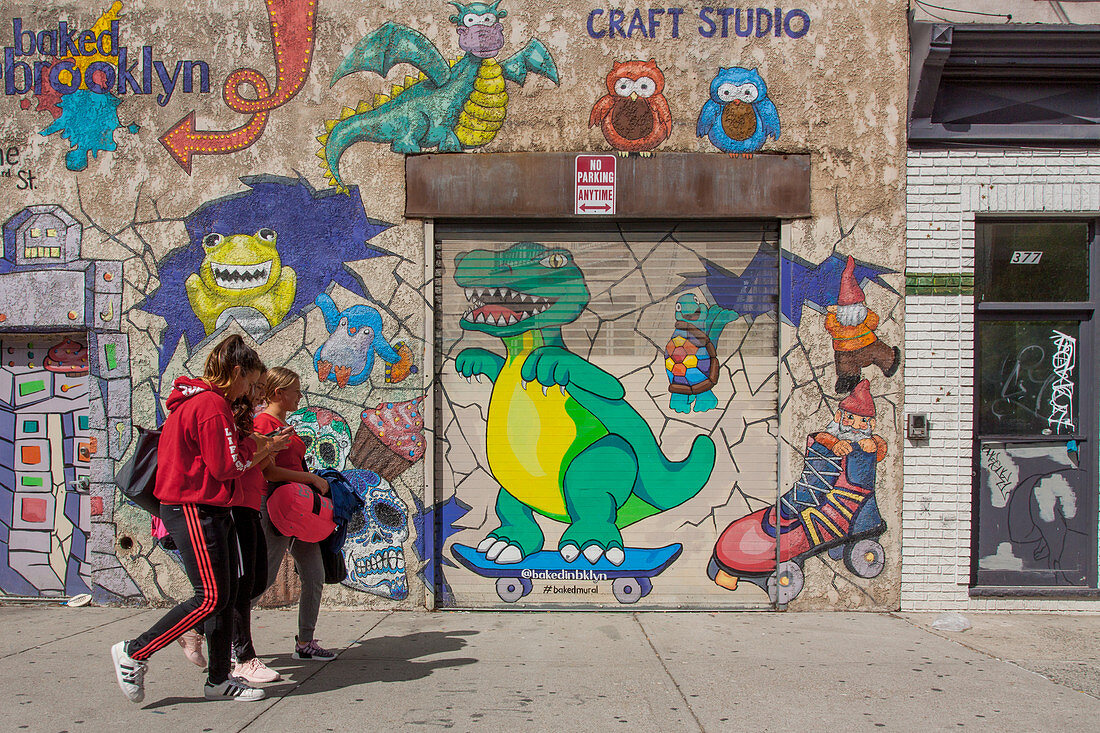 GIRLS PASSING IN FRONT OF A GRAFFITI-COVERED WALL IN A NEIGHBORHOOD IN BROOKLYN, NEW YORK CITY, NEW YORK, UNITED STATES, USA
