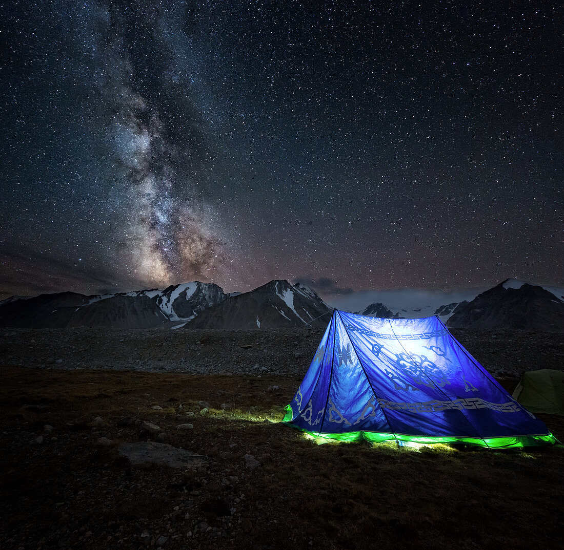 Beleuchtetes mongolisches Zelt vor dem Nachthimmel und einer leuchtenden Milchstraße, Berg Khuiten-Basislager, Altai-Gebirge im Hintergrund, Bayan-Olgii-Provinz, Mongolei