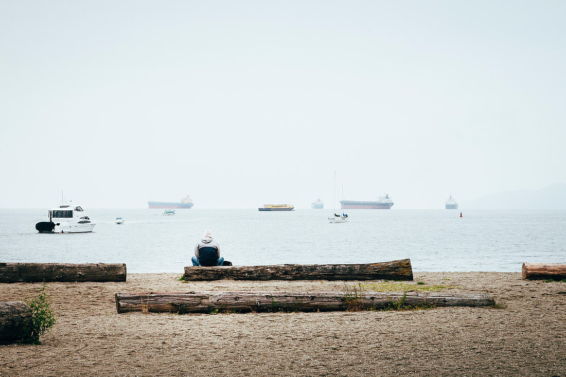 Vancouver, man sitting on tree trunk in English Bay during rain, Canada