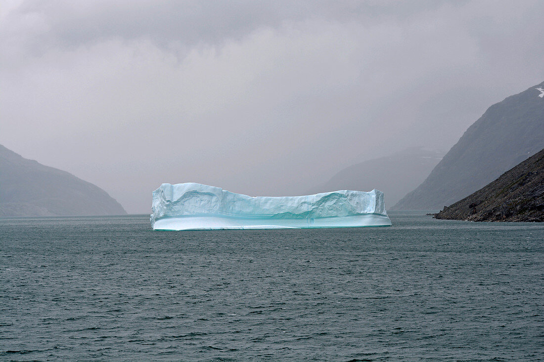 Greenland; Prins Christian Sund; impressive passage on the southern tip of the island; turquoise blue iceberg; bad weather; Rain clouds cover the mountains in the sound